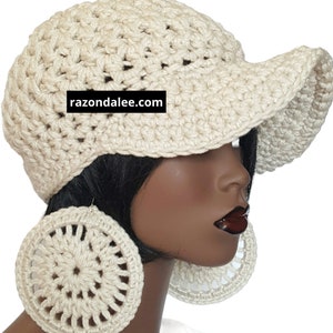 May include: A cream-coloured crocheted cap with a wide brim and a black rectangular label featuring the white text razondalee.com. The cap is paired with large, circular, cream-coloured crocheted earrings with a radial pattern.