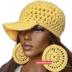 May include: A bright yellow crocheted baseball cap with a textured stitch pattern and a matching pair of large, circular crocheted earrings. The image includes the text razondalee.com in a small red rectangular box near the centre.