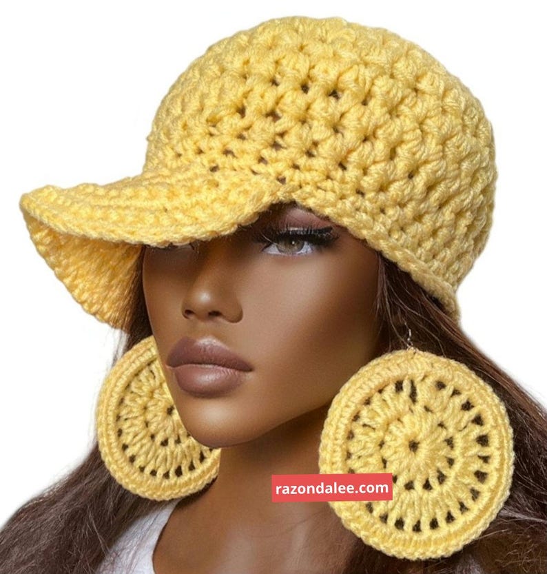 May include: A bright yellow crocheted baseball cap with a textured stitch pattern and a matching pair of large, circular crocheted earrings. The image includes the text razondalee.com in a small red rectangular box near the centre.
