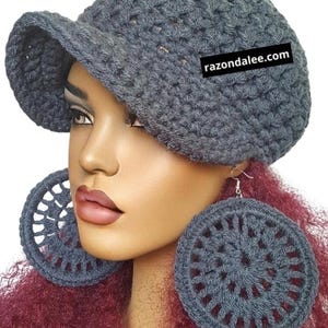 May include: A dark grey crocheted newsboy cap with a short brim and a black rectangular tag featuring the white text razondalee.com, paired with large, circular, dark grey crocheted hoop earrings with a radial openwork pattern.