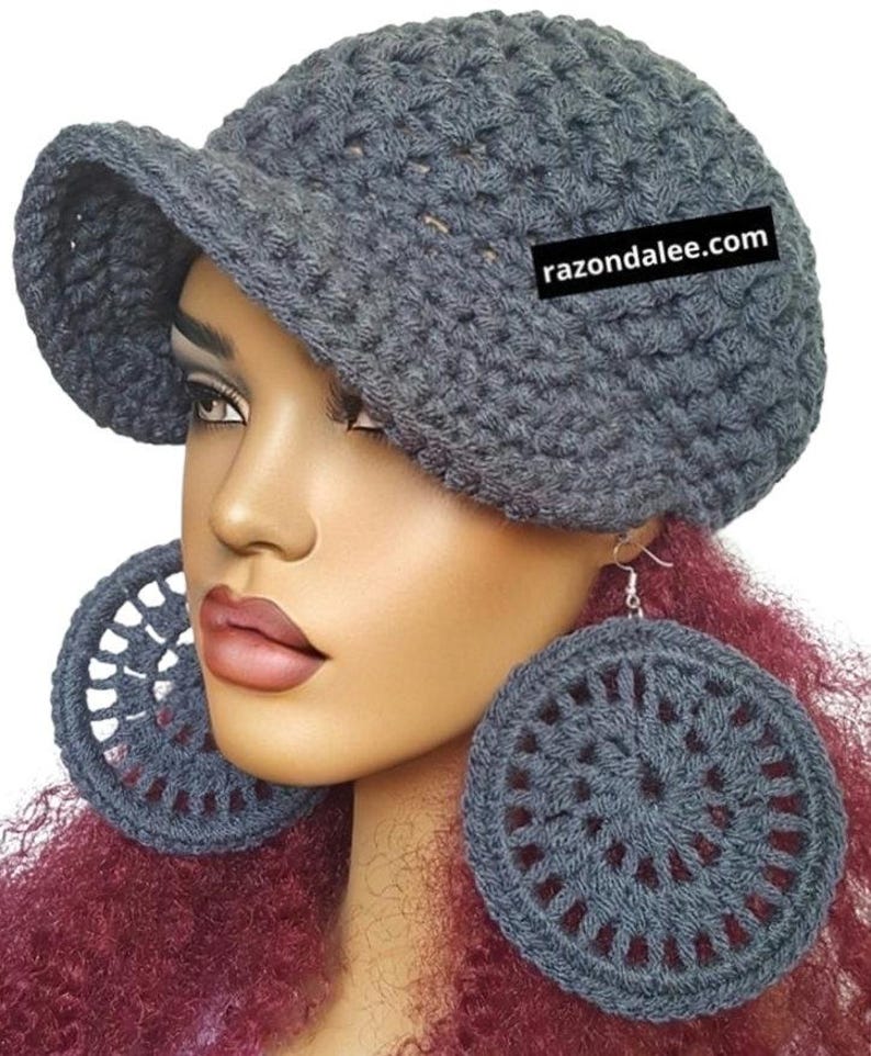 May include: A dark grey crocheted newsboy cap with a short brim and a black rectangular tag featuring the white text razondalee.com, paired with large, circular, dark grey crocheted hoop earrings with a radial openwork pattern.