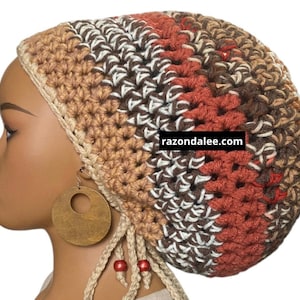 May include: A crocheted beanie in shades of brown, tan, white, and rust orange with a textured stitch pattern. The hat features dangling cords with red beads and displays the text razondalee.com on a black rectangular label on the side.