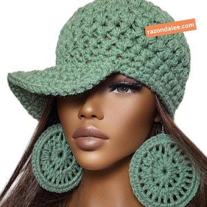 May include: A sage green crocheted baseball cap with a textured stitch pattern and a matching pair of large, circular crocheted earrings. An orange rectangular tag on the cap features the white text razondalee.com.