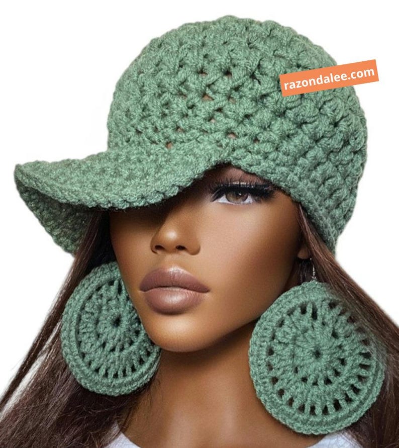 May include: A sage green crocheted baseball cap with a textured stitch pattern and a matching pair of large, circular crocheted earrings. An orange rectangular tag on the cap features the white text razondalee.com.