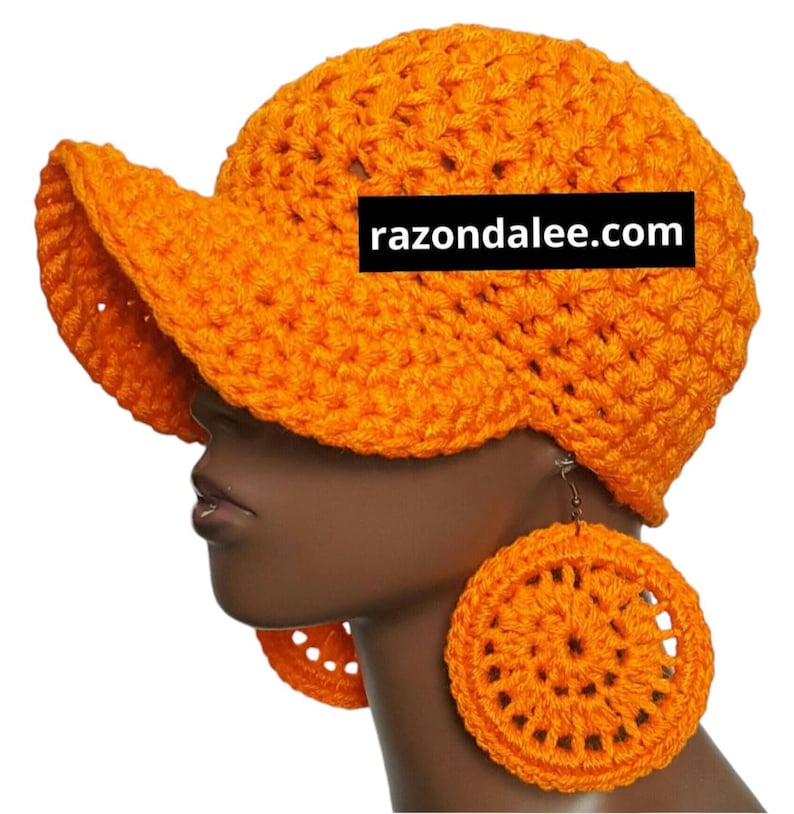 May include: Bright orange crochet hat with a visor and matching circular earrings. The hat and earrings are made of a thick, textured yarn. The website razondalee.com is printed on the hat.