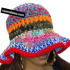 May include: A colorful, handmade crochet bucket hat. The hat features a vibrant mix of colors including red, blue, orange, purple, and green. The brim is trimmed in red. The text "razondalee.com" is printed on a black rectangle on the hat.