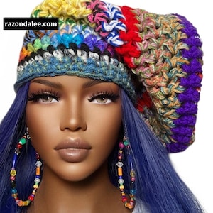 May include: A colorful, hand-crocheted beret in a vibrant mix of rainbow hues. The hat features a textured stitch pattern and a blue brim. The website razondalee.com is visible on the hat. The model is wearing large hoop earrings.