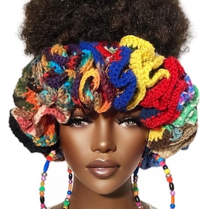 May include: A multi-colored crochet headband featuring a dense, ruffled texture in shades of yellow, red, blue, green, and purple. The accessory is worn around the head, paired with large hoop earrings decorated with small, multi-colored plastic beads.