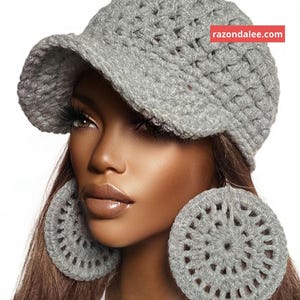 May include: A grey crocheted newsboy cap with a structured brim and a pair of matching large circular crocheted earrings. The cap features a red rectangular tag with the white text razondalee.com on the upper right side.