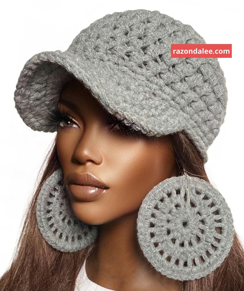 May include: A grey crocheted newsboy cap with a structured brim and a pair of matching large circular crocheted earrings. The cap features a red rectangular tag with the white text razondalee.com on the upper right side.