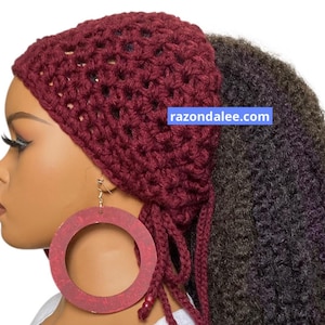 May include: A deep burgundy crochet head wrap featuring an open-knit pattern with dangling ties and beads. The accessory is displayed on a mannequin head alongside a large, circular, textured red earring. The text razondalee.com is visible.