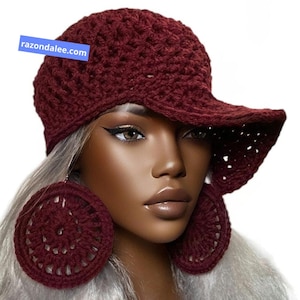 May include: A deep burgundy crochet baseball cap and matching large circular crochet earrings. The cap features a textured, open-stitch pattern and a wide brim. A blue rectangular tag with the white text razondalee.com is visible.
