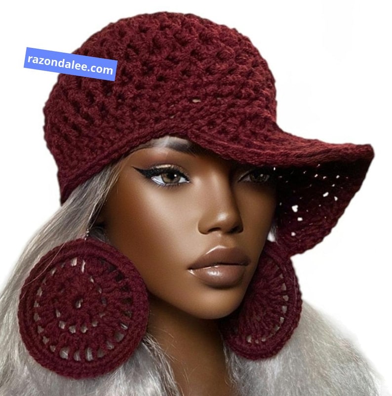 May include: A deep burgundy crochet baseball cap and matching large circular crochet earrings. The cap features a textured, open-stitch pattern and a wide brim. A blue rectangular tag with the white text razondalee.com is visible.