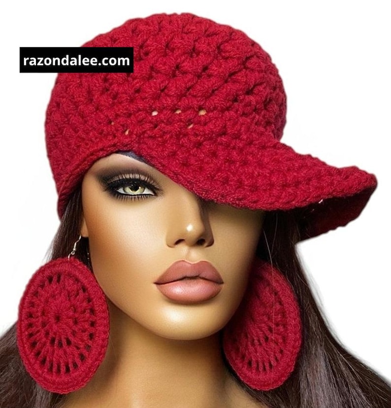 May include: A deep red crocheted baseball cap and matching large circular crocheted dangle earrings. The cap features a textured yarn pattern and a prominent brim. The text razondalee.com is visible in a black box on the cap.