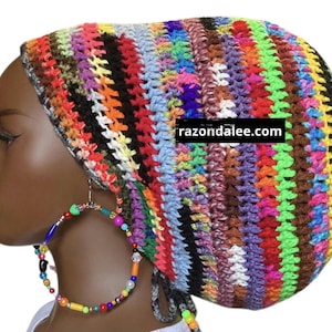 May include: A colorful, handmade crochet hat with a striped pattern in various colors, including red, orange, green, and blue. The hat is worn with large hoop earrings adorned with colorful beads. The website razondalee.com is visible on the hat.