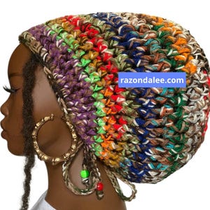May include: A multi-colored crochet beanie featuring a vibrant mix of purple, green, orange, blue, and brown yarn. The hat includes dangling braided ties with small green and red beads. The text razondalee.com is visible on the side of the beanie.
