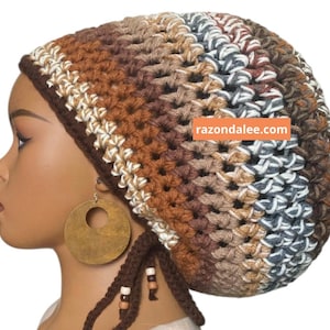 May include: A crocheted beanie featuring horizontal stripes in shades of brown, tan, cream, and grey. The hat has a dark brown border and two dangling brown ties adorned with small wooden beads. The text razondalee.com is visible on the side.