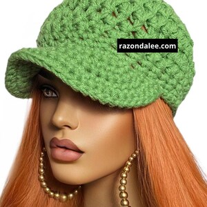 May include: A light green crocheted newsboy cap with a small brim. The hat is made of a chunky yarn and has a textured appearance. The text "razondalee.com" is visible on the hat.
