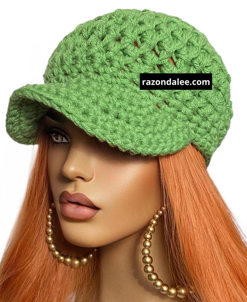 May include: A light green crocheted newsboy cap with a small brim. The hat is made of a chunky yarn and has a textured appearance. The text "razondalee.com" is visible on the hat.