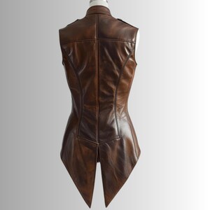 Pu&ograve; includere: Un gilet in pelle marrone con una vestibilit&agrave; sartoriale, caratterizzato da un colletto alla coreana e un design a schiena divisa. Il gilet ha una silhouette aderente ed &egrave; esposto su un manichino. La pelle ha un aspetto invecchiato.