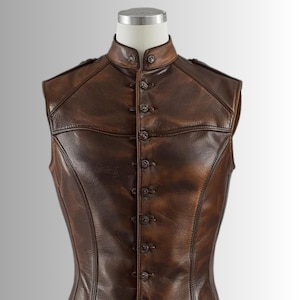Pu&ograve; includere: Un gilet in pelle marrone con collo alto e chiusura a bottoni. Il gilet ha una vestibilit&agrave; sartoriale e presenta cuciture decorative e dettagli sulle spalle. La pelle ha un aspetto invecchiato, con variazioni di colore e consistenza.