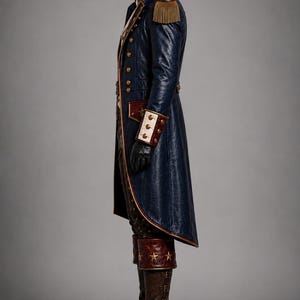 Puede incluir: Un abrigo largo azul oscuro con charreteras doradas, botones de lat&oacute;n y pu&ntilde;os blancos. El abrigo tiene cuello alto y ribetes rojos. Pantalones oscuros metidos en botas de cuero marr&oacute;n con hebillas y detalles de estrellas doradas.