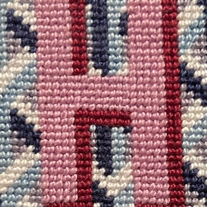 Puede incluir: Primer plano de un diseño de punto de cruz con la letra "H" en rosa con detalles burdeos. El fondo es una mezcla de puntadas azules, blancas y celeste, creando un efecto texturizado.