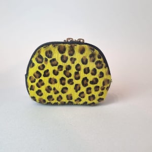 May include: A small, semi-circular coin purse featuring a vibrant yellow and black leopard print pattern on a textured, hair-on-hide material. The pouch is secured with a black zipper closure along the top edge, featuring metallic hardware.