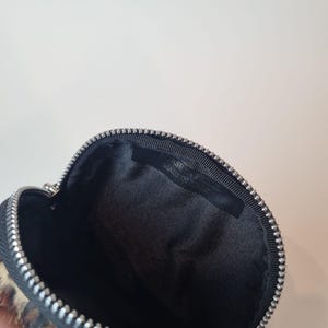 May include: A small, round, zippered pouch featuring a leopard print pattern on the exterior. The interior is lined with black fabric and includes a black tag with the text BORSE IN PELLE MADE IN ITALY stitched inside the top edge.