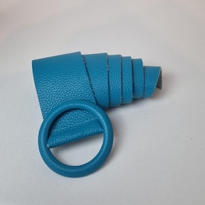 May include: A rolled turquoise leather strip with a matching circular buckle. The leather has a textured surface, suitable for belts or accessories. The buckle is a simple, round design. The leather is a vibrant shade of turquoise.