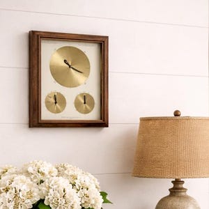 May include: A cozy entryway scene featuring a wooden console table with a woven basket of white flowers. A framed clock hangs above, and a lamp with a tan shade sits on the table. A straw hat and umbrella add to the welcoming decor.