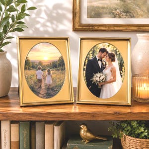 May include: Two rectangular gold picture frames with oval-shaped inner openings. The left frame displays a photograph of two children walking in a field at sunset. The right frame displays a photograph of a bride and groom standing together.