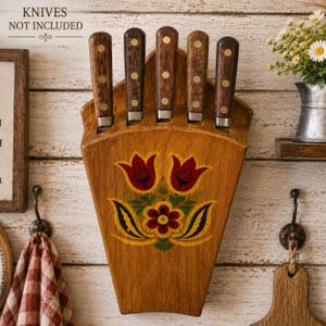 May include: A wall-mounted wooden knife block with five slots, featuring a hand-painted floral design with red tulips and yellow leaves. The block has a light brown finish and includes the text KNIVES NOT INCLUDED at the top left corner.