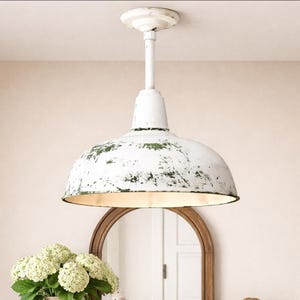 May include: White, dome-shaped pendant light with a distressed finish. The light fixture has a green and white speckled pattern and a long, white stem. The light is suspended from the ceiling and is above a wooden-framed mirror.