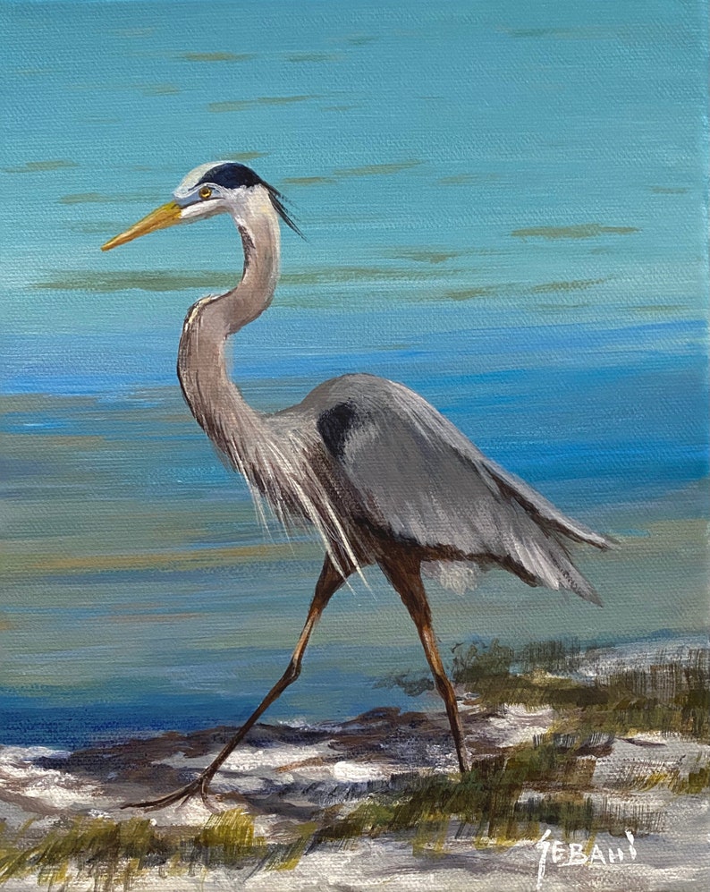 May include: An acrylic painting of a Great Blue Heron in a coastal setting. The bird is depicted in profile, with grey and white feathers, a long neck, and a yellow beak. The background features a blue sky and water, with a sandy shore.