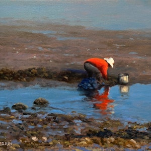 May include: A person in a red shirt and white hat bends over to pick up something from the water. The person is standing in shallow water with a bucket beside them. The water is blue and the ground is brown.