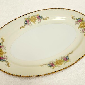 Pu&ograve; includere: Piatto ovale da portata con superficie color crema e bordo dorato. Il piatto &egrave; decorato con disegni floreali gialli, rosa e blu. Il bordo ha un motivo geometrico nero e oro.