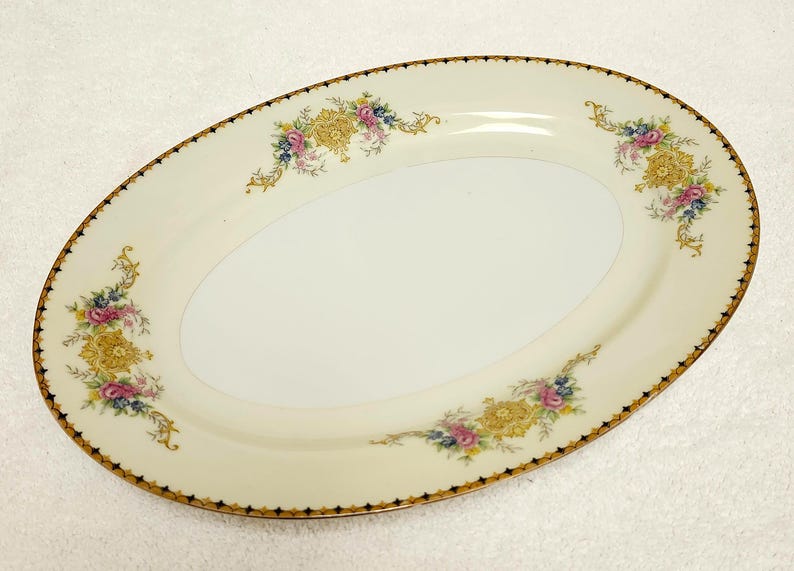 Pu&ograve; includere: Piatto ovale da portata con superficie color crema e bordo dorato. Il piatto &egrave; decorato con disegni floreali gialli, rosa e blu. Il bordo ha un motivo geometrico nero e oro.