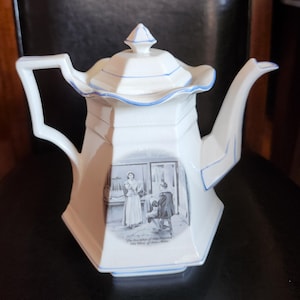 May include: White porcelain teapot with a hexagonal body and a lid. The teapot has blue trim and a handle. A black and white illustration of a scene with two people is on the front. The text on the teapot reads "The Description of John's Salon".