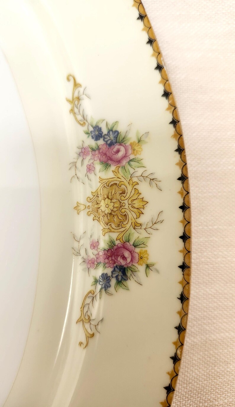 Pu&ograve; includere: Piatto in porcellana color crema con un motivo floreale. Il piatto presenta fiori rosa, blu e gialli con accenti dorati e un bordo decorativo dorato e nero. Un pezzo classico per servire.