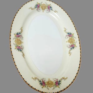 Pu&ograve; includere: Piatto ovale da portata con sfondo color crema e centro bianco. Il bordo presenta un bordo oro e nero. Disegni floreali in rosa, blu e oro adornano il piatto.