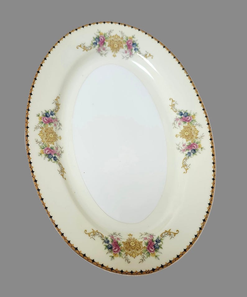 Pu&ograve; includere: Piatto ovale da portata con sfondo color crema e centro bianco. Il bordo presenta un bordo oro e nero. Disegni floreali in rosa, blu e oro adornano il piatto.