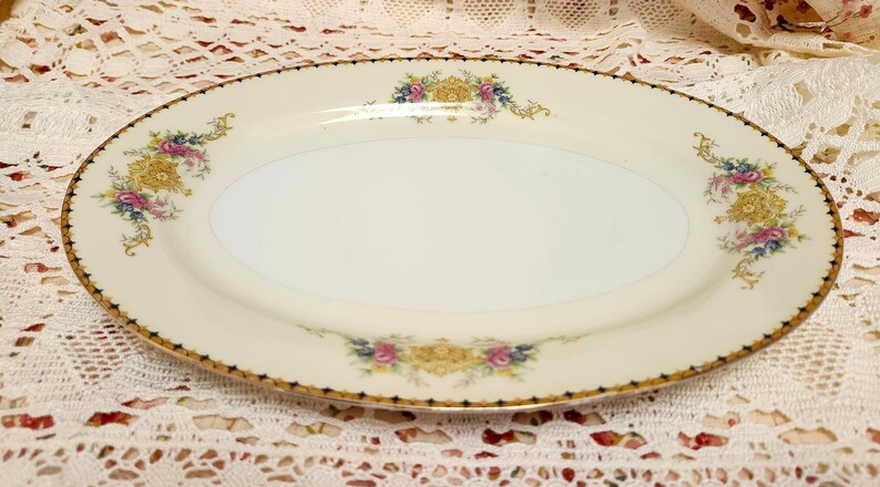 Pu&ograve; includere: Un piatto da portata ovale color crema con bordo dorato e decorazioni floreali. Il piatto presenta un delicato disegno di fiori dorati, rosa, blu e gialli. Il bordo &egrave; rifinito con un motivo a pois neri.