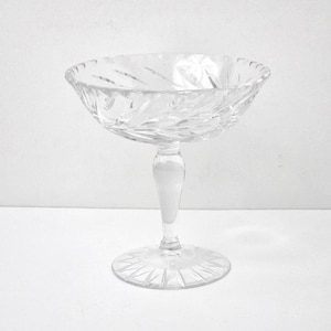 May include: A clear, stemmed glass dessert bowl with a wide, textured rim and a decorative, patterned base. The bowl is made of crystal and is designed for serving desserts or other small portions. The bowl stands approximately 6 inches tall.