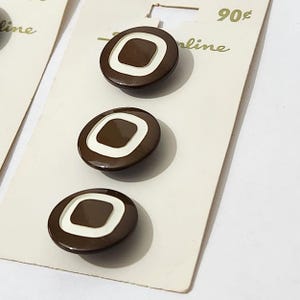 May include: Three brown and white plastic buttons with a square design. The buttons are on a white card with the text "90¢" and "line" printed on it.