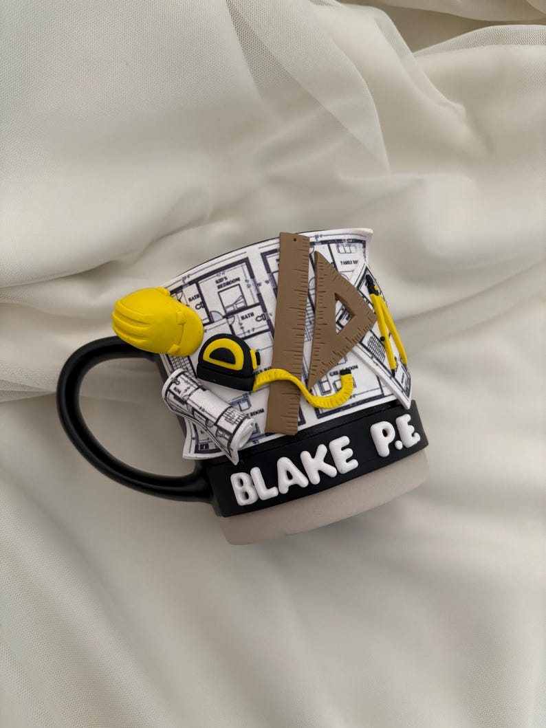Puede incluir: Una taza de cer&aacute;mica con asa y base negras, con una superficie blanca decorada con un patr&oacute;n de planos. Los elementos 3D incluyen un casco amarillo, una cinta m&eacute;trica, una regla marr&oacute;n, una escuadra y el texto en blanco BLAKE P.E.