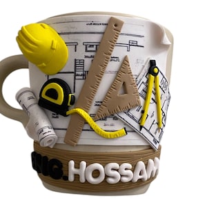 Puede incluir: Una taza de cerámica beige con una base de madera marrón. La taza está decorada con un diseño de plano, un casco amarillo, una regla, un transportador, una brújula y una cinta métrica. La base de la taza tiene el texto "Eng. Hossam" en letras blancas y negras.