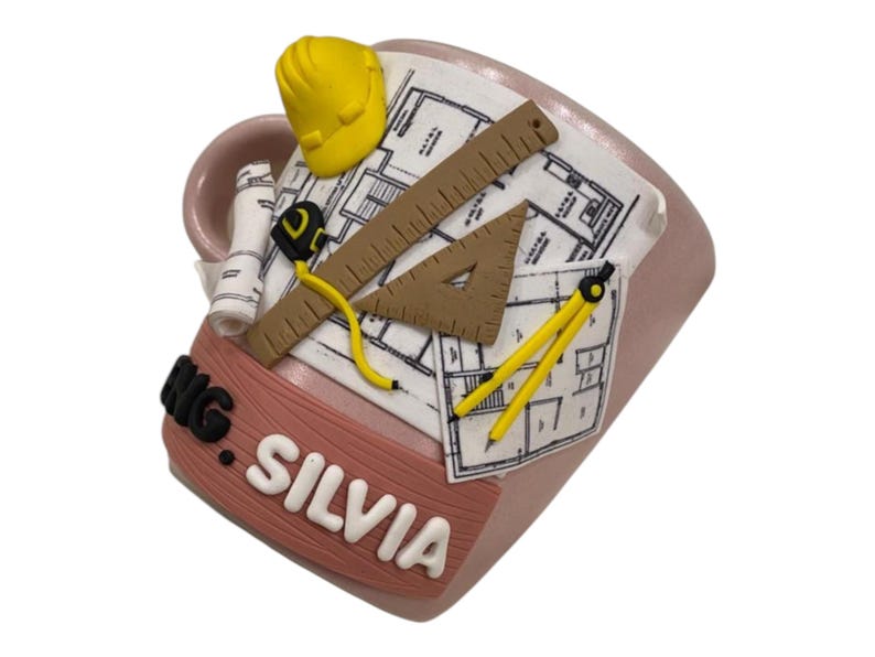Puede incluir: Una taza de cer&aacute;mica rosa claro con un dise&ntilde;o en relieve 3D de un casco de seguridad amarillo, un plano enrollado, una regla marr&oacute;n, un tri&aacute;ngulo marr&oacute;n, una cinta m&eacute;trica amarilla y un comp&aacute;s amarillo. La taza muestra el texto ENG. SILVIA en letras blancas.