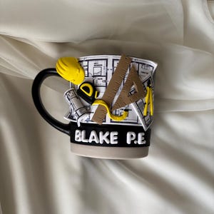 Puede incluir: Una taza de cer&aacute;mica en blanco y negro con un dise&ntilde;o arquitect&oacute;nico en 3D que incluye un casco amarillo, una cinta m&eacute;trica, una regla triangular y un comp&aacute;s. La taza muestra un patr&oacute;n de plano y el texto blanco BLAKE P.E. en una banda negra.