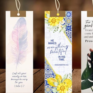 May include: Five rectangular paper bookmarks with string loops at the top. Designs include a feather, yellow lemons with blue tiles, a green leaf, blue floral patterns, and a misty forest. Each features religious text including Bible verses.